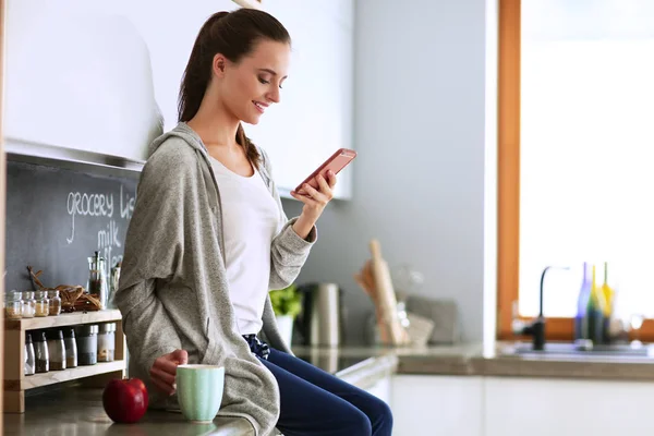 Mujer usando el teléfono móvil sentado en la cocina moderna — Foto de Stock