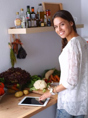Mutfakta yemek yapmak için tablet bilgisayar kullanan genç bir kadın.