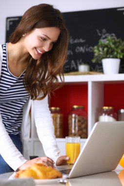 Dizüstü bilgisayar kullanarak ve mutfakta oturmuş çekici genç kadın