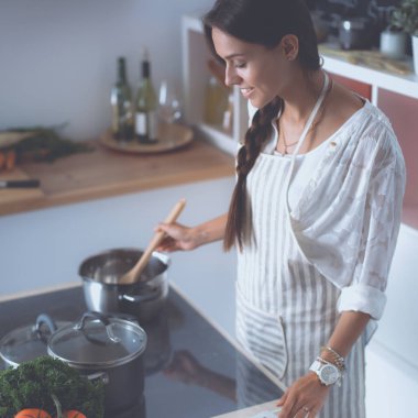 Mutfakta yemek yapmak için tablet bilgisayar kullanan genç bir kadın.