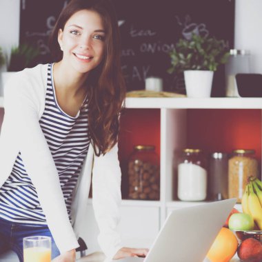 Dizüstü bilgisayar kullanarak ve mutfakta oturmuş çekici genç kadın