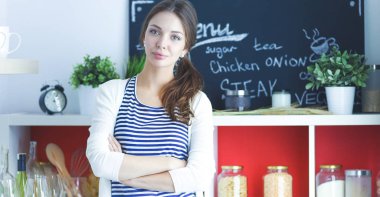 Genç bir kadın mutfakta duruyor.