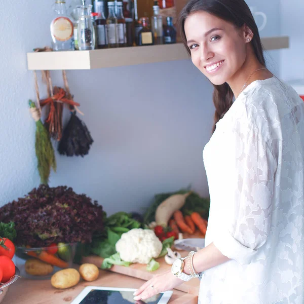 Ung kvinna använder en surfplatta dator för att laga mat i sitt kök — Stockfoto