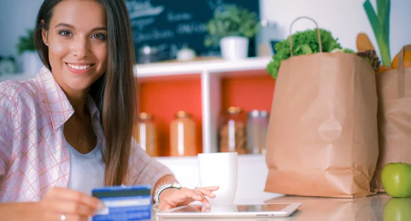 Femme souriante achats en ligne en utilisant tablette et carte de crédit dans la cuisine — Photo