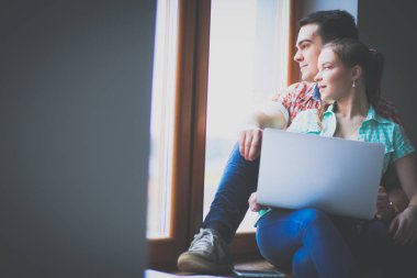 Dizüstü bilgisayar ile pencere evde oturan hareketli Çift
