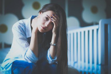 Yatakta çocuk karyolası yakın oturan genç yorgun kadın