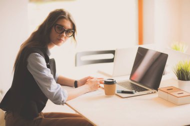 Ofis masasında dizüstü bilgisayarıyla oturan genç bir kadın.