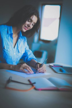 Ofis masasında dizüstü bilgisayarıyla oturan genç bir kadın.