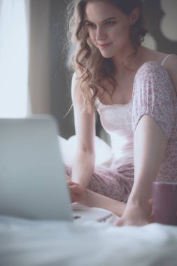 Dizüstü bilgisayar ile yatakta oturan genç güzel kadın