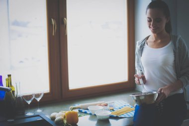 Genç bir kadın mutfakta krep pişiriyor sobanın yanında duruyor.