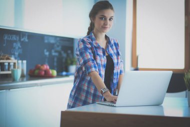 Mutfakta dizüstü bilgisayar kullanan genç bir kadın.