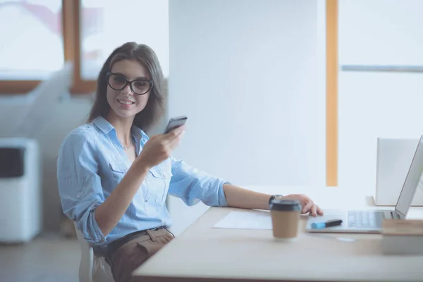 Mulher de negócios jovem bonita sentada na mesa do escritório e falando no telefone celular — Fotografia de Stock