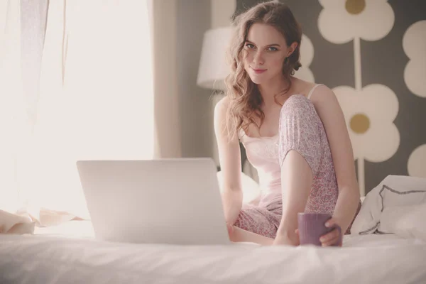 Young beautiful woman sitting in bed with laptop — Stock Photo, Image