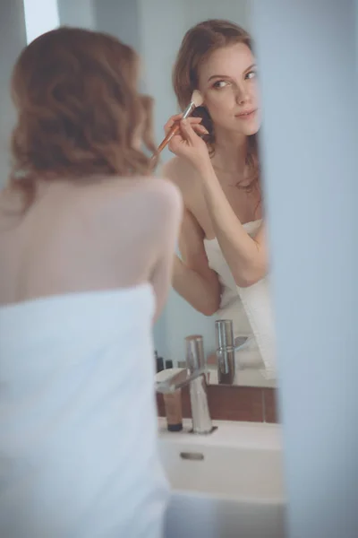 Jovem mulher olhando no espelho e colocando maquiagem em — Fotografia de Stock