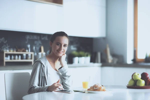 Mujer joven con jugo de naranja y tableta en la cocina —  Fotos de Stock