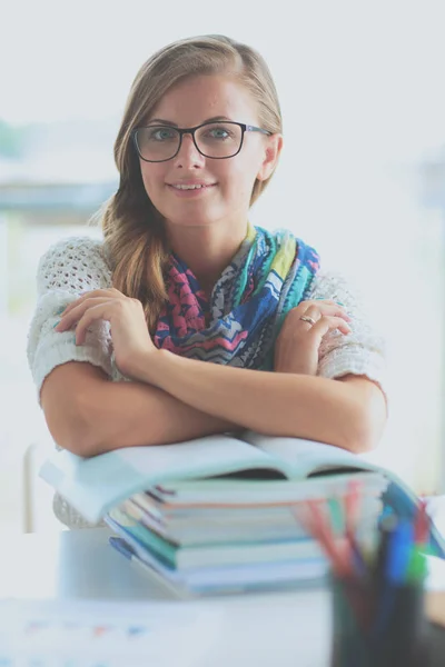 Jonge vrouw zit aan een bureau tussen de boeken — Stockfoto