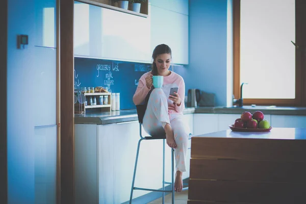 Woman using mobile phone sitting in modern kitchen — Stock Photo, Image