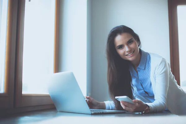 Jeune femme debout près du bureau avec ordinateur portable — Photo