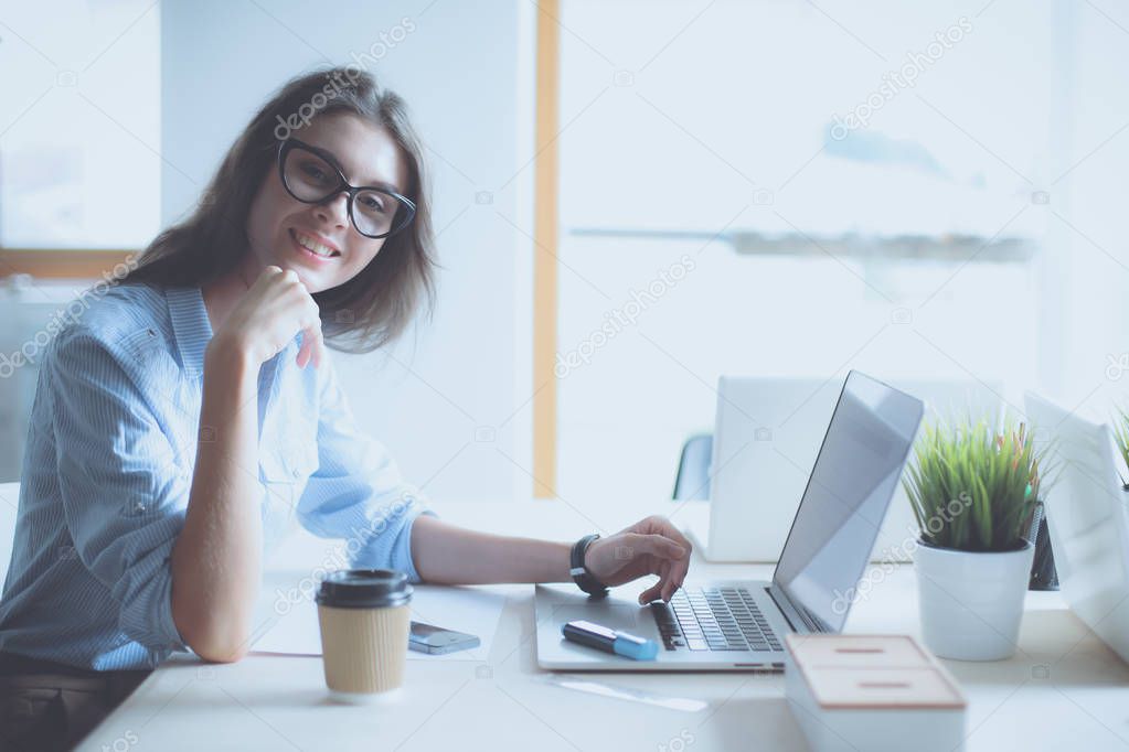 Young woman sitting at office table with laptop