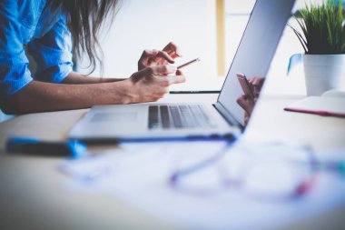 Ofis masasında dizüstü bilgisayarıyla oturan genç bir kadın.