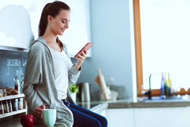 modern mutfakta otururken cep telefonu kullanan kadın