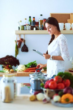 Mutfakta yemek yapmak için tablet bilgisayar kullanan genç bir kadın.