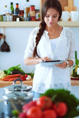 Mutfakta yemek yapmak için tablet bilgisayar kullanan genç bir kadın.
