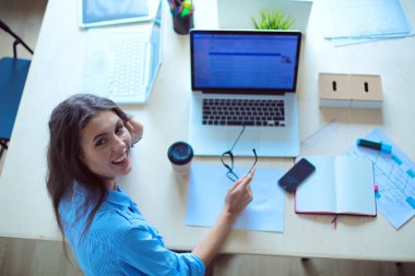 Ofis masasında dizüstü bilgisayarıyla oturan genç bir kadın.