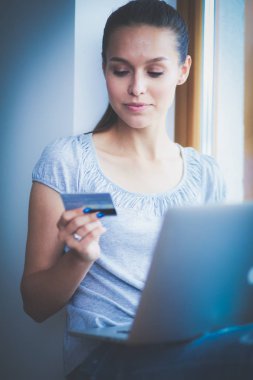 Genç ve güzel bir kadın evde dizüstü bilgisayar kullanıyor.