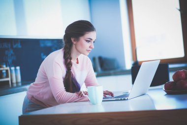 Mutfakta dizüstü bilgisayar kullanan genç bir kadın.