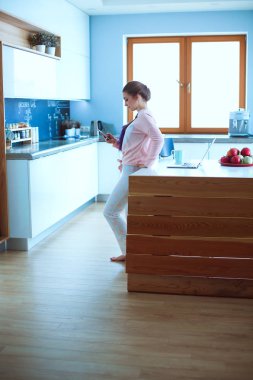 Cep telefonu ayakta modern mutfak kullanan kadın