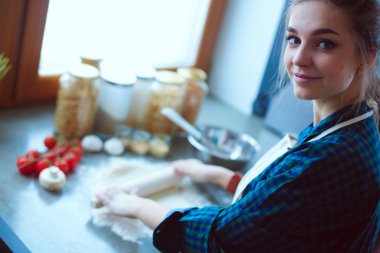 Güzel bir kadın mutfakta pasta pişiriyor. Masanın yanında duruyor.