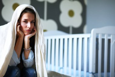 Yatakta çocuk karyolası yakın oturan genç yorgun kadın