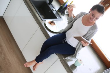 Mutfakta dijital tablet kullanan güzel genç bir kadın.