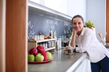 Genç bir kadın mutfakta tablet kullanıyor ve kahve içiyor.