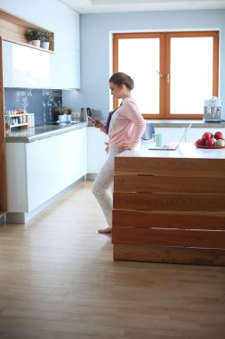 Cep telefonu ayakta modern mutfak kullanan kadın