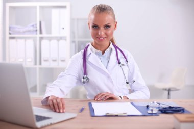 Güzel, genç, gülümseyen bayan doktor masada oturuyor ve yazıyor..