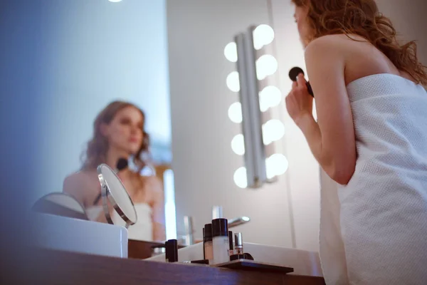 Молодая женщина смотрит в зеркало и наносит макияж — стоковое фото