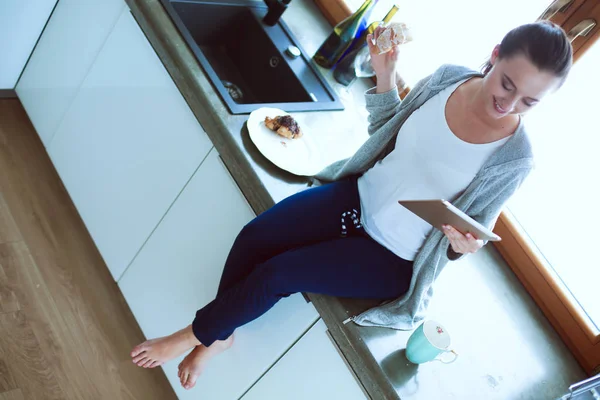Hermosa joven usando una tableta digital en la cocina — Foto de Stock