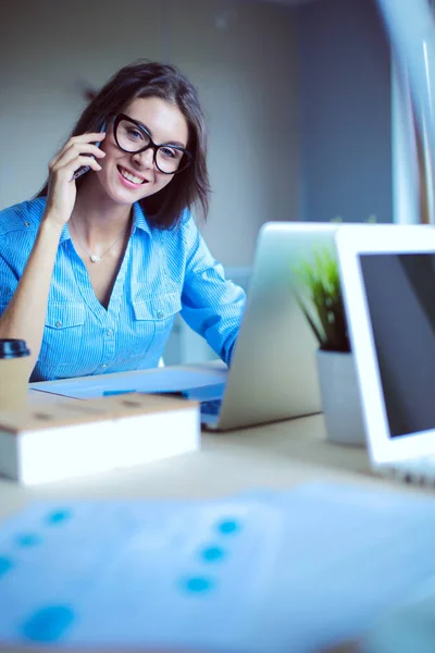 Hermosa joven mujer de negocios sentada en el escritorio de la oficina y hablando por teléfono celular —  Fotos de Stock