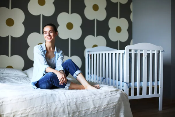 Jonge vrouw zittend op het bed in de buurt van childrens kinderbed — Stockfoto