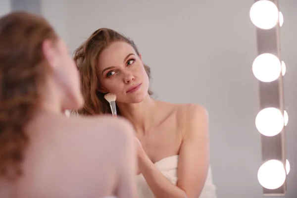 Молода жінка дивиться у дзеркало і одягає макіяж — стокове фото