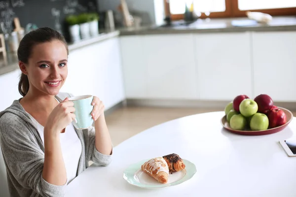 Kobieta, picie herbaty z słodkiego rogalika na stole w kuchni — Zdjęcie stockowe