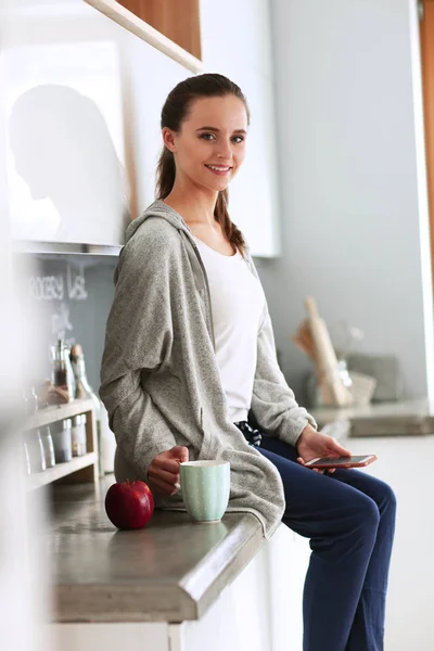 Kvinna med mobiltelefon sitter i moderna kök — Stockfoto