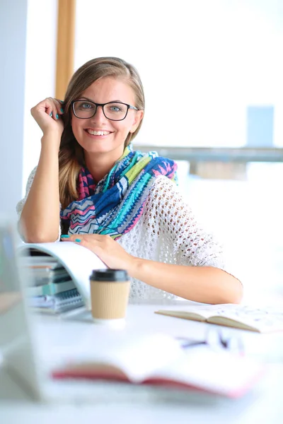 Young woman sitting at a desk among books — Stock Photo, Image