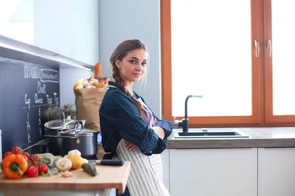 Egy fiatal nő áll a tűzhely mellett a konyhában. — Stock Fotó