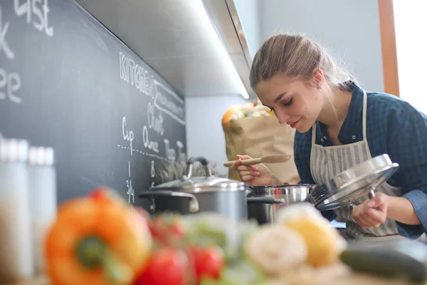 Mujer joven cocinando en su cocina de pie cerca de la estufa — Foto de Stock