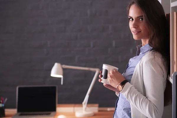 Portret ontspannen jonge vrouw zitten aan haar bureau met een kopje koffie — Stockfoto