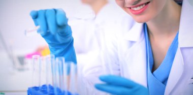 Kadın araştırmacı, beyaz arka planda izole edilmiş ilaç şişeleri ve mataralarla çevrili.