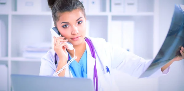 Doctora joven estudiando imagen de rayos X sentada en el escritorio —  Fotos de Stock